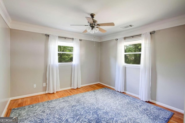 empty room with a ceiling fan, wood finished floors, ornamental molding, and visible vents