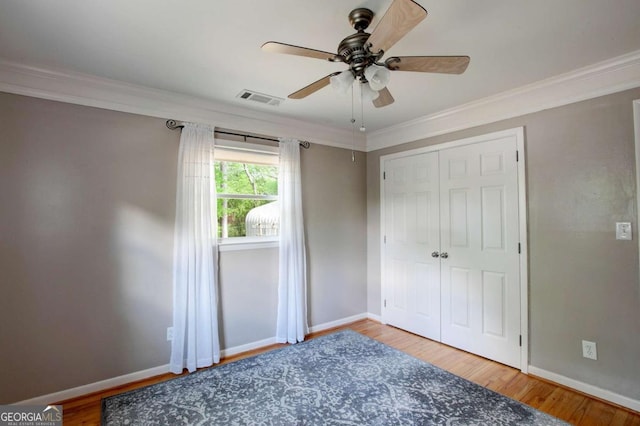 unfurnished bedroom featuring crown molding, a closet, visible vents, wood finished floors, and baseboards