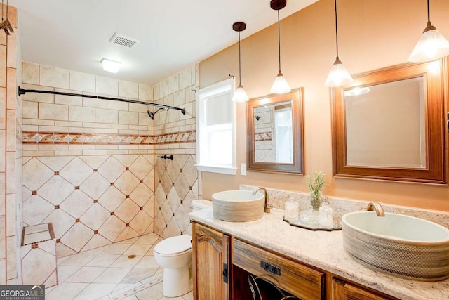 full bath with a tile shower, visible vents, toilet, washer / dryer, and double vanity