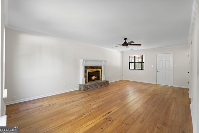 unfurnished living room with baseboards, a brick fireplace, a ceiling fan, crown molding, and light wood finished floors