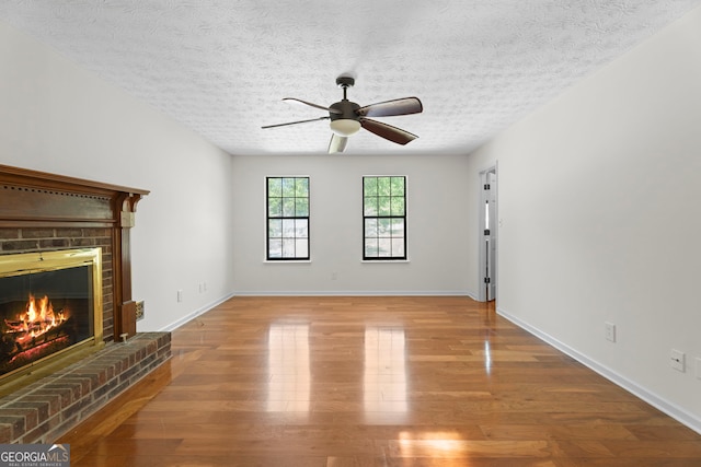 unfurnished living room featuring a brick fireplace, ceiling fan, a textured ceiling, and wood finished floors