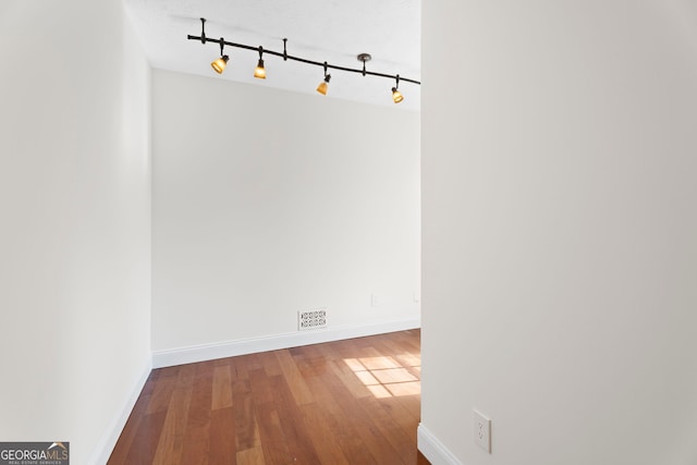 interior space with rail lighting, wood-type flooring, and baseboards