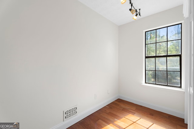 unfurnished room featuring track lighting, wood finished floors, baseboards, and visible vents