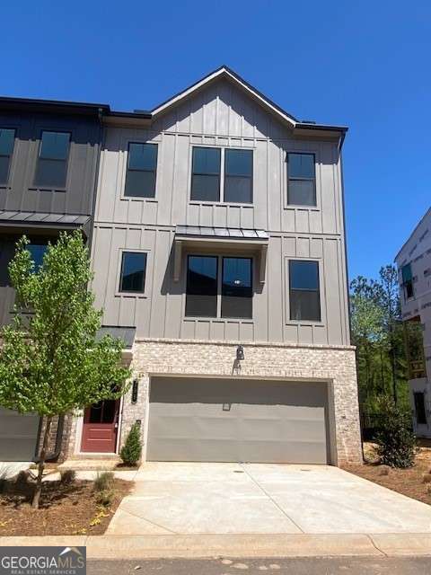 view of front of house with an attached garage, board and batten siding, driveway, and stone siding