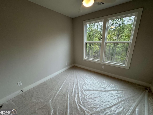empty room with a wealth of natural light, carpet flooring, baseboards, and a ceiling fan