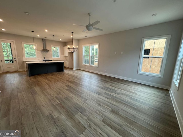 unfurnished living room featuring ceiling fan with notable chandelier, dark wood-type flooring, recessed lighting, a sink, and baseboards
