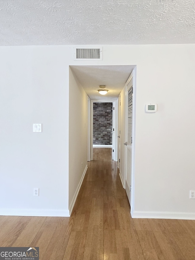 hallway featuring a textured ceiling, wood finished floors, baseboards, and visible vents