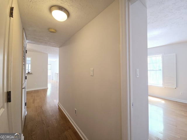 hall featuring a textured ceiling, wood finished floors, and a wealth of natural light