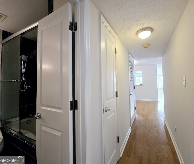 hallway featuring baseboards, wood finished floors, and a textured ceiling