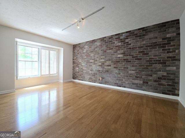 empty room with brick wall, a textured ceiling, wood finished floors, and baseboards