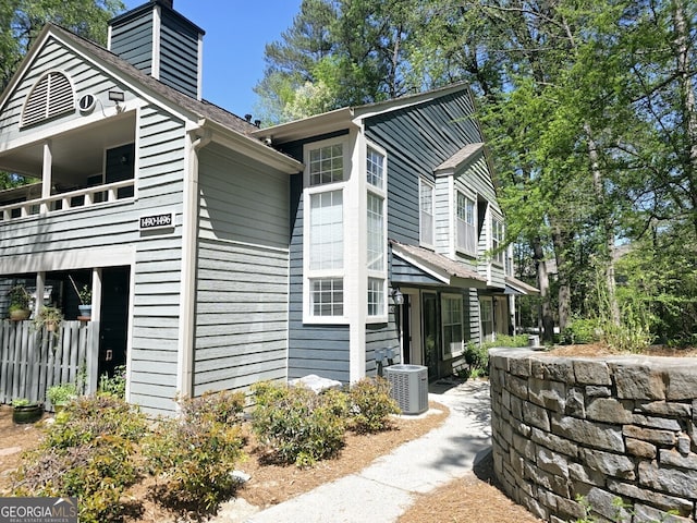 view of side of property featuring central AC unit, a balcony, and a chimney