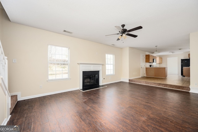 unfurnished living room featuring dark wood finished floors, baseboards, a fireplace with raised hearth, and ceiling fan
