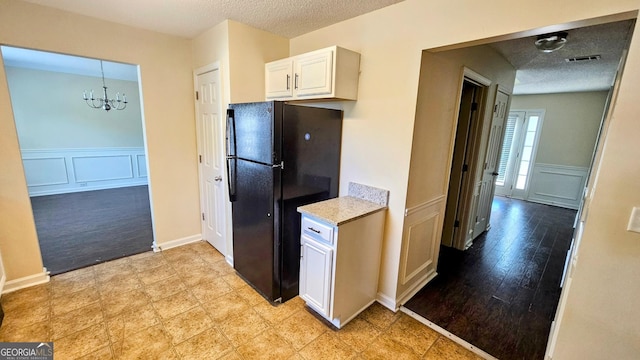 kitchen featuring freestanding refrigerator, a textured ceiling, visible vents, a decorative wall, and a chandelier