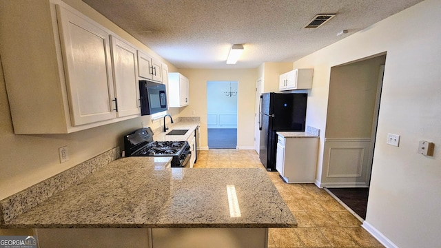 kitchen featuring light stone countertops, visible vents, a sink, a peninsula, and black appliances