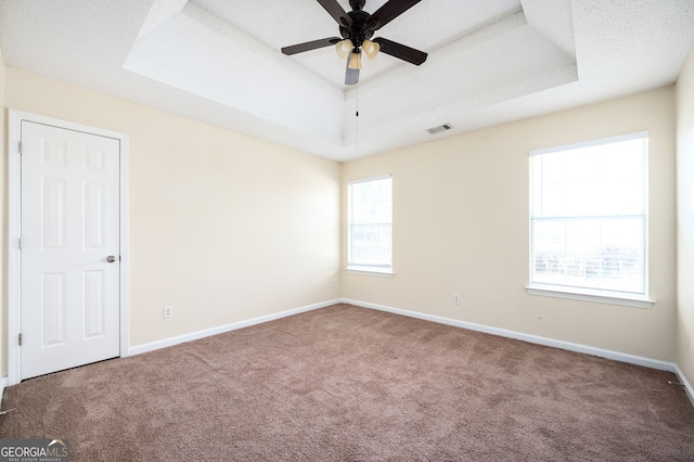 carpeted spare room with baseboards, a raised ceiling, ceiling fan, and visible vents