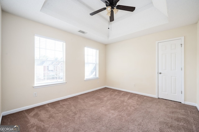 carpeted empty room with baseboards, a raised ceiling, ceiling fan, and visible vents