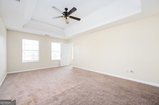 carpeted empty room with a tray ceiling, visible vents, baseboards, and ceiling fan