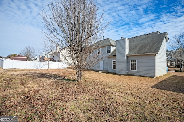 rear view of property featuring roof with shingles, fence, and a chimney