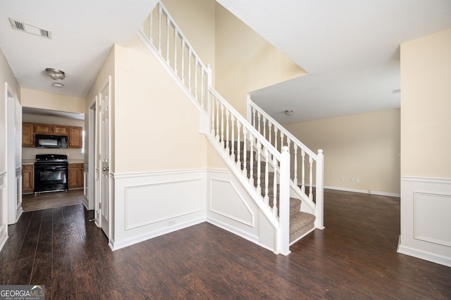 staircase featuring a decorative wall, a wainscoted wall, visible vents, and wood finished floors