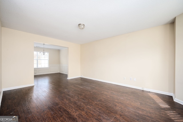 spare room with a chandelier, dark wood-style flooring, and baseboards