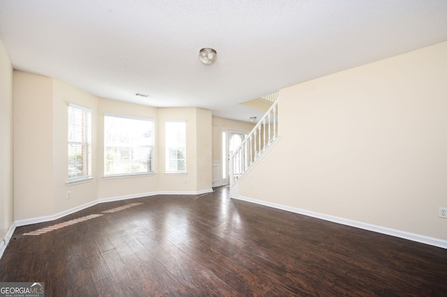 unfurnished living room with baseboards, stairs, dark wood finished floors, and visible vents