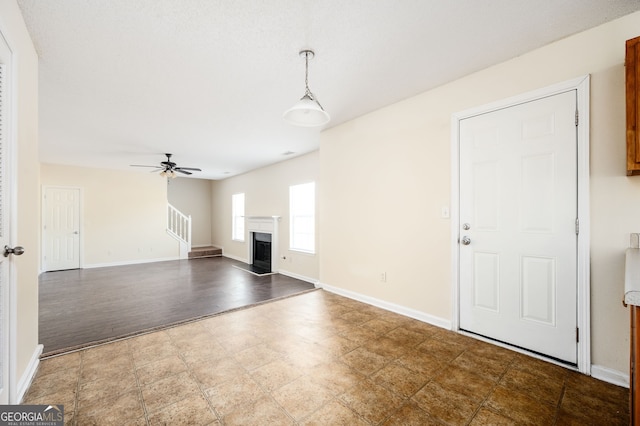 unfurnished living room featuring a fireplace, baseboards, a ceiling fan, and stairway