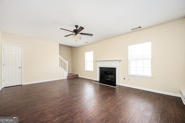 unfurnished living room with a fireplace with raised hearth, stairway, ceiling fan, dark wood-style floors, and baseboards
