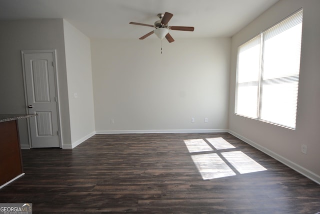 empty room featuring baseboards, a ceiling fan, and dark wood finished floors