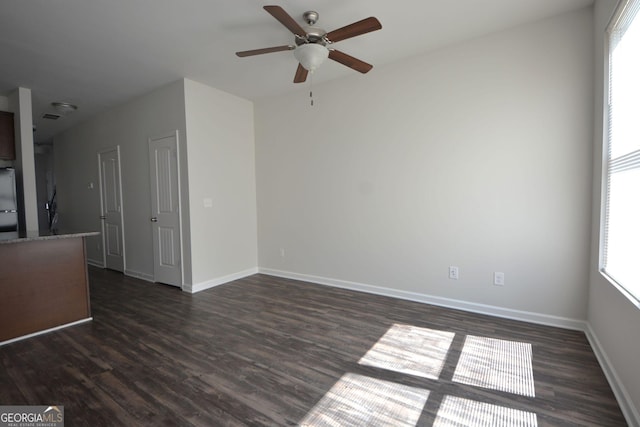 unfurnished living room featuring a wealth of natural light, ceiling fan, baseboards, and dark wood finished floors