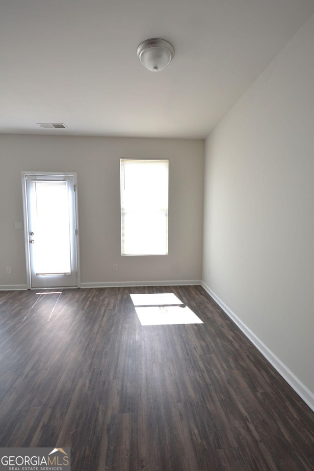 spare room with visible vents, baseboards, dark wood finished floors, and plenty of natural light