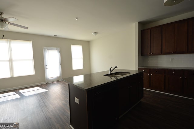 kitchen featuring a sink, ceiling fan, a kitchen island with sink, dark wood-type flooring, and decorative backsplash