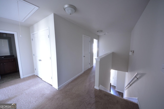 hall with light carpet, an upstairs landing, baseboards, and attic access
