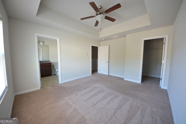 unfurnished bedroom with a tray ceiling, light colored carpet, baseboards, and a walk in closet