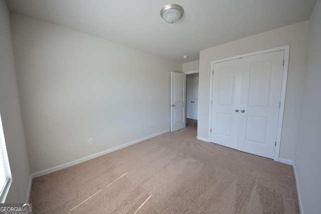 unfurnished bedroom with light carpet, a closet, and baseboards
