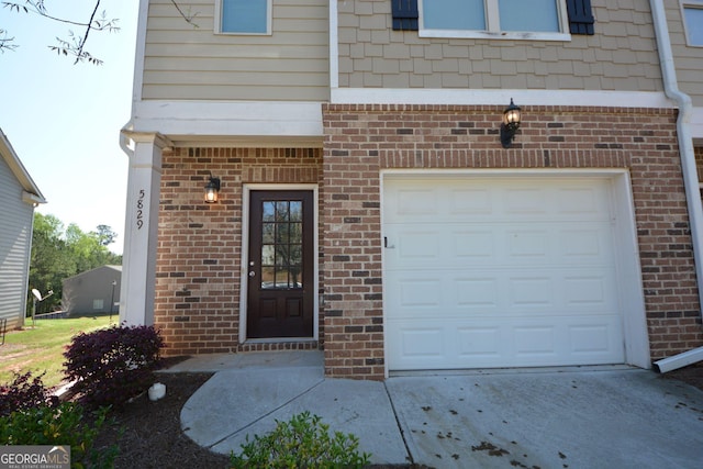 doorway to property with a garage, concrete driveway, and brick siding