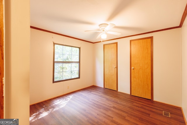unfurnished bedroom with visible vents, multiple closets, wood finished floors, and crown molding