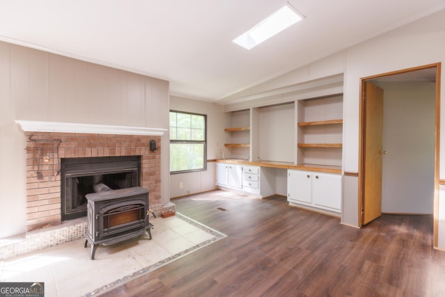 unfurnished living room with vaulted ceiling, built in study area, a wood stove, dark wood finished floors, and ornamental molding