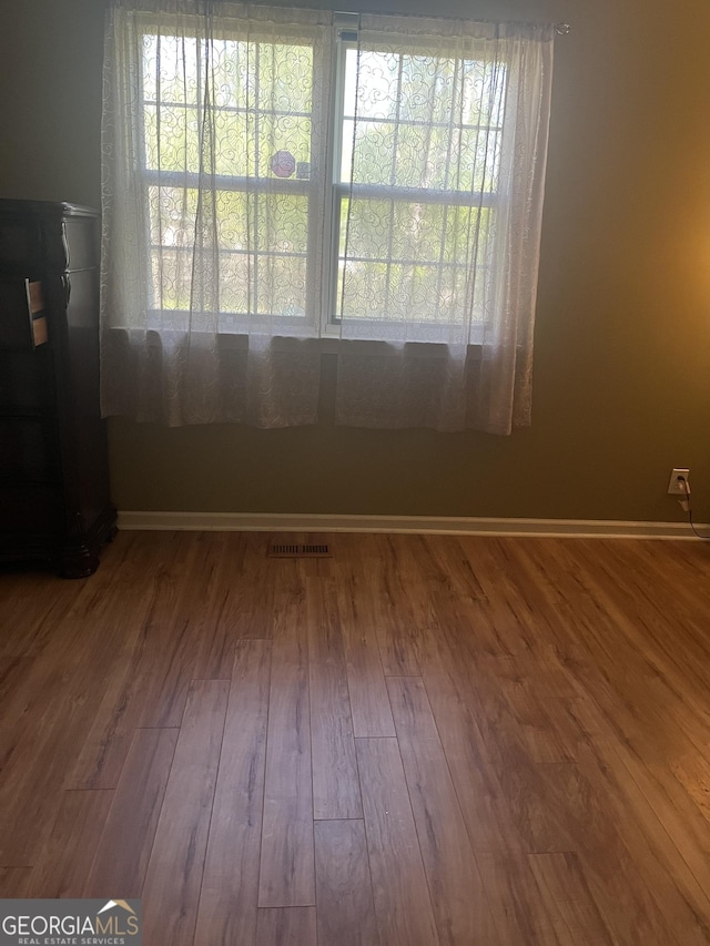 empty room with wood finished floors, visible vents, and plenty of natural light