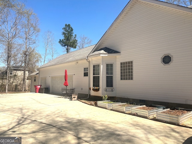 rear view of house featuring a garden, roof with shingles, and concrete driveway