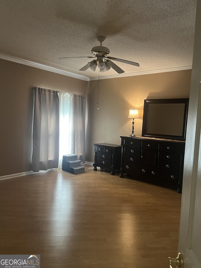 bedroom with baseboards, a textured ceiling, crown molding, and wood finished floors