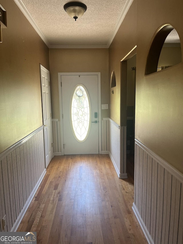 doorway with ornamental molding, a wainscoted wall, wood finished floors, and a textured ceiling