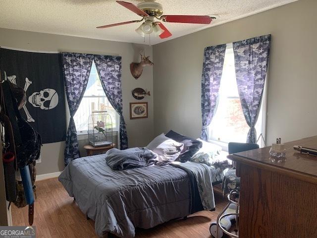 bedroom with ceiling fan, wood finished floors, and a textured ceiling