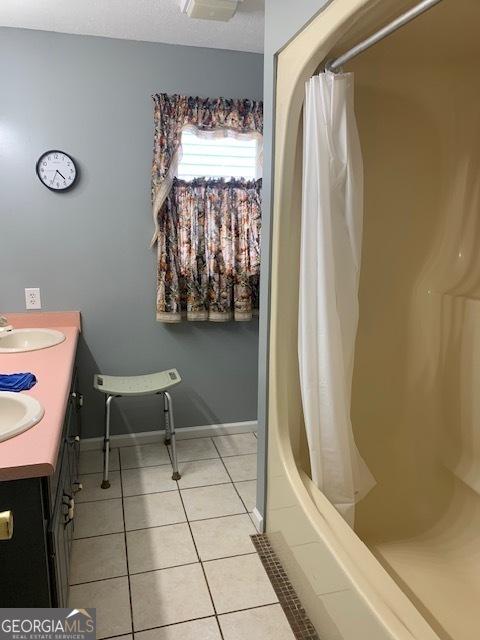 bathroom featuring baseboards, double vanity, tile patterned flooring, a shower with curtain, and a sink
