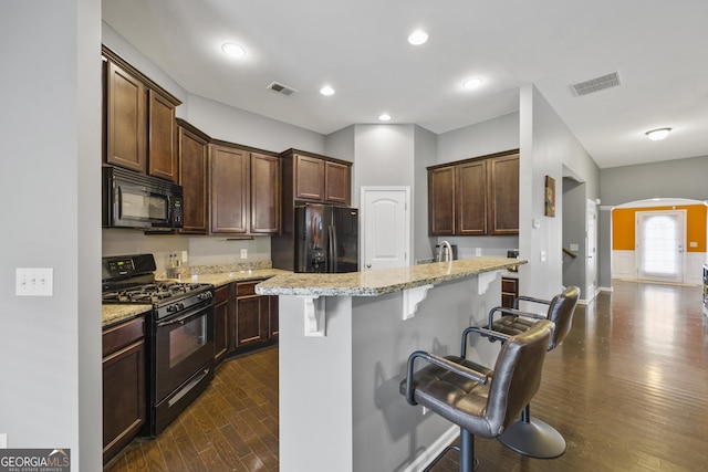 kitchen featuring light stone countertops, dark wood-type flooring, a kitchen bar, visible vents, and black appliances