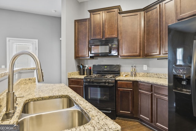 kitchen featuring a sink, dark wood-style flooring, black appliances, and light stone countertops