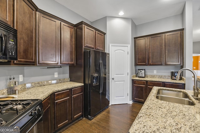 kitchen with light stone countertops, a sink, black appliances, and dark wood-type flooring