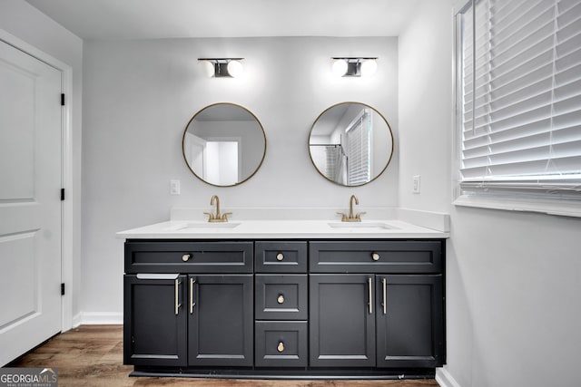 full bath featuring double vanity, wood finished floors, baseboards, and a sink