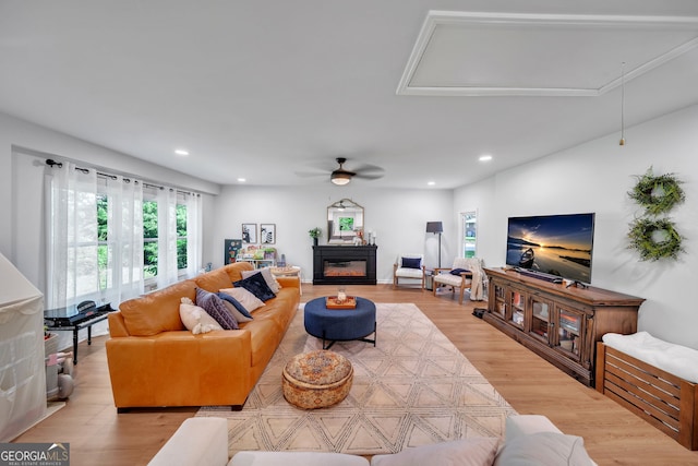 living room featuring recessed lighting, light wood finished floors, a ceiling fan, attic access, and a glass covered fireplace