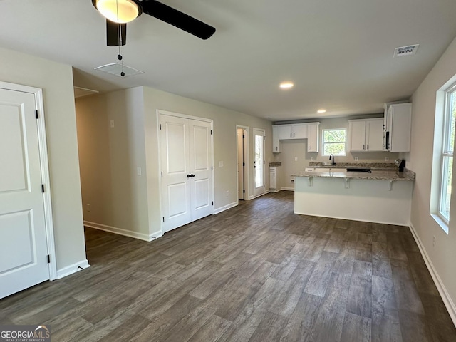 kitchen featuring a ceiling fan, a peninsula, dark wood-style flooring, light stone countertops, and visible vents
