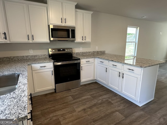 kitchen with white cabinets, stainless steel appliances, a peninsula, and dark wood-type flooring